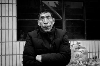 一位老人站在一栋建筑前 手里拿着一个袋子。