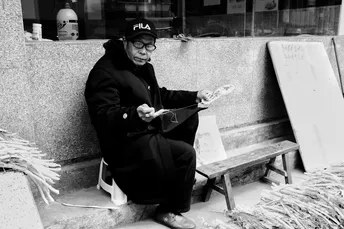 一个老人坐在长凳上读报纸