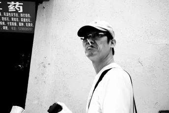 一个黑白照片 一位老妇人正在街上走 戴着帽子 拿着一个包 站在一个停车计时器旁边。