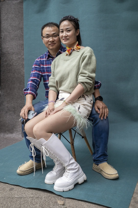 一个年轻男子坐在椅子上 双腿交叉 一个年轻女子在为拍照摆姿势。