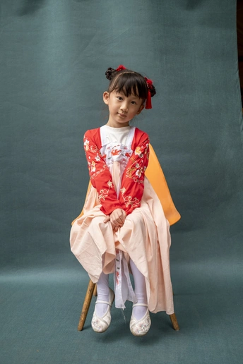 一个穿着中国传统服装的年轻女孩坐在小椅子上 穿着红白相间的裙子。