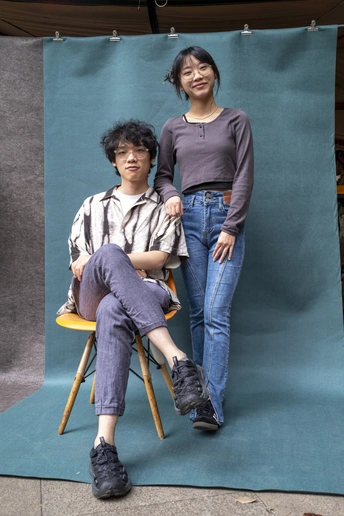 一个年轻女子坐在蓝色的椅子上 一个年轻男子站在她身后。