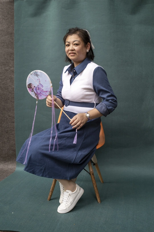 一位穿着传统服装的年轻女子坐在绿色背景前的椅子上。