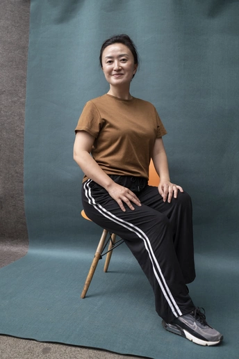 一位穿着棕色衬衫和黑色裤子的年轻女子坐在椅子上 双腿交叉。