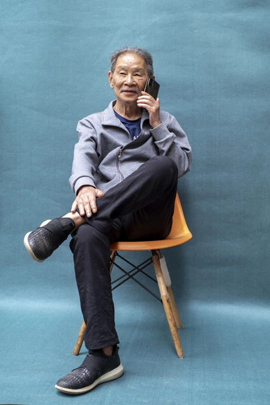 一个穿着蓝色衣服的老年男子坐在蓝色的椅子上 正在打电话。