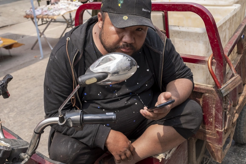 一个坐在摩托车上的男人旁边有一个装满鱼的推车。