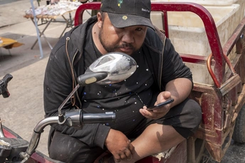 一个坐在摩托车上的男人旁边有一个装满鱼的推车。