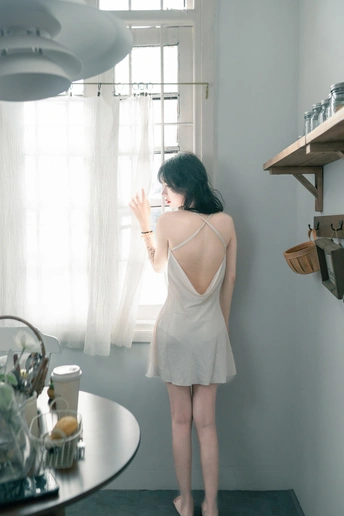 一个穿白裙子的女人站在厨房里 朝窗外看