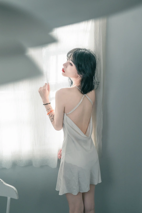 一位穿着白色连衣裙的年轻女子正在窗户旁向外看