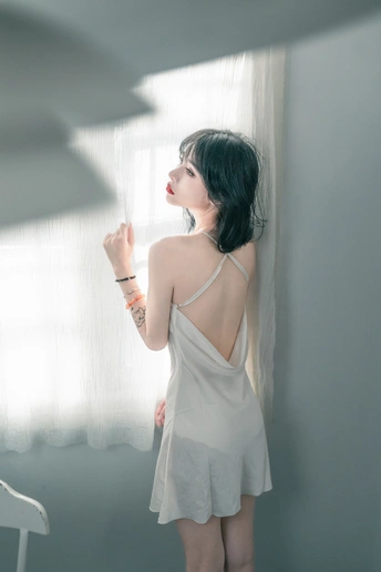 一位穿着白色连衣裙的年轻女子正在窗户旁向外看