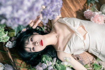 一个穿着白色连衣裙的年轻女子躺在草地上 周围环绕着花。