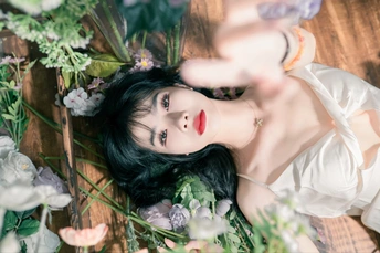 一个穿着白色裙子的美丽女人躺在地板上 周围有花和草。