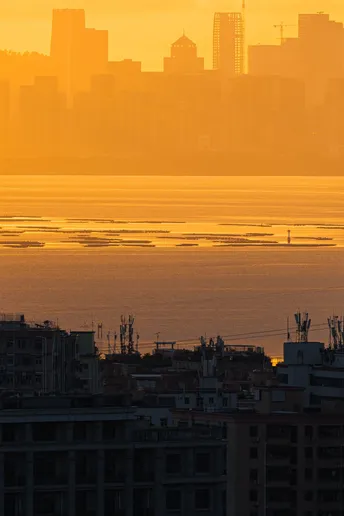 太阳落在一个城市天际线前的水域上。