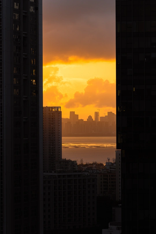 太阳正在城市的天际线上落下 周围有高大的建筑和一扇大窗户。