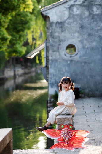 一个小女孩坐在运河边 带着一把红色的雨伞 坐在水边。