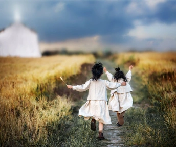 两个穿白色连衣裙的女孩沿着田地小径跑过 背景有一座谷仓。