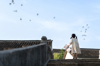 一个穿着白色连衣裙的女人走在楼梯上 天空中一群鸟儿飞翔。