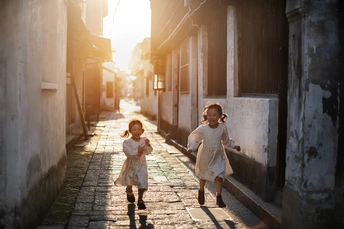 两个穿着白色衣服的小女孩沿着一条狭窄的街道跑下来