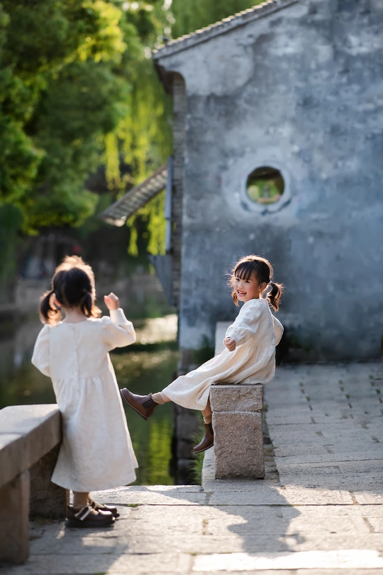 一个穿着白色连衣裙的小女孩握着另一个小女孩的手 她们站在一个小池塘上的桥上。