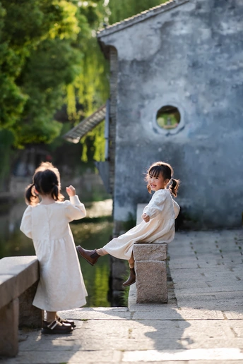 一个穿着白色连衣裙的小女孩握着另一个小女孩的手 她们站在一个小池塘上的桥上。