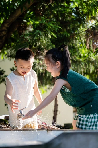 一个小男孩和一个小女孩在喷泉里玩水。