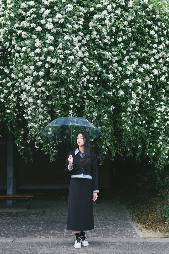 一位女士拿着黑色雨伞站在一棵开满白色花朵的树前