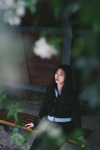 一个穿着黑色衣服的年轻女子坐在一棵大树旁的木凳上