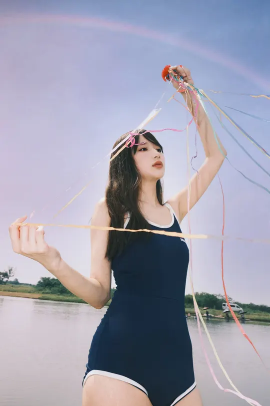 穿着泳装的年轻女子在水上附近的海滩上持风筝站立
