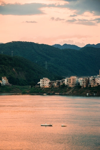 一艘小船漂浮在一个靠近城市和山丘的大型水体上