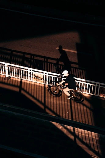 一个人骑自行车在夜晚的街道上 有一个人物的影子在围栏上。