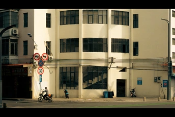 一个街角 有一座大型白色建筑 人们骑着自行车和摩托车。