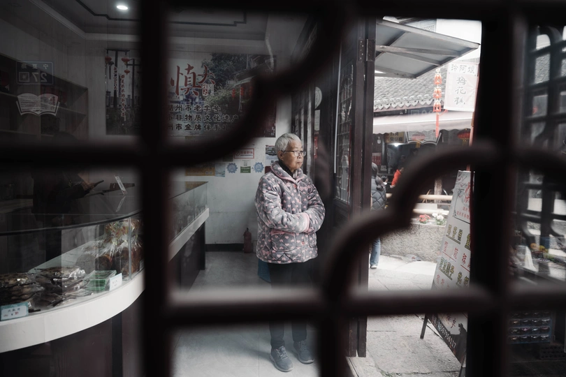 一位老妇人在商店门口站着 透过窗户向外看。