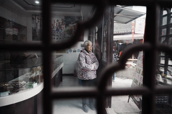 一位老妇人在商店门口站着 透过窗户向外看。