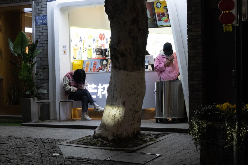 夜晚街道上 一个人坐在树下的长椅上 一家商店里 一个人坐在人行道上。