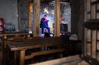 一个男子站在一个有木制桌子和长凳的房间里 一个女子坐在桌子旁。