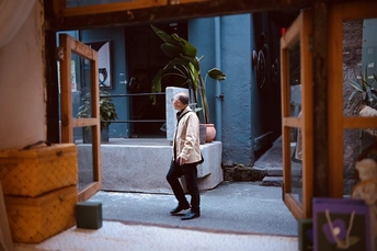 一位妇女走在蓝色建筑前的人行道上 门上有一个植物。