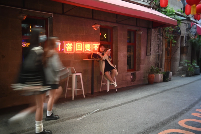 一位站在人行道上 前方有红氖灯餐厅 旁边有人经过的女人。