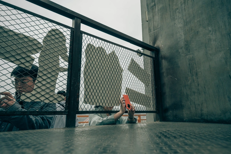 一个人拿着滑板正在给一只鸟拍照 另一个人坐在栅栏的另一边。