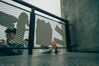 一个人拿着滑板正在给一只鸟拍照 另一个人坐在栅栏的另一边。