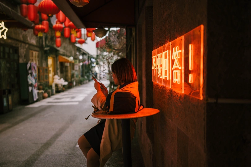 一个年轻女子手提一篮红灯笼走在巷子里 另一个人站在墙上拿着盘子。