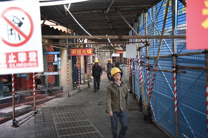 一个戴安全帽的男人走在靠近脚手架和标志的人行道上。