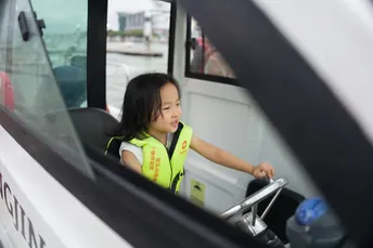 一个穿着背心的年轻女孩驾驶一辆小公共汽车或小船