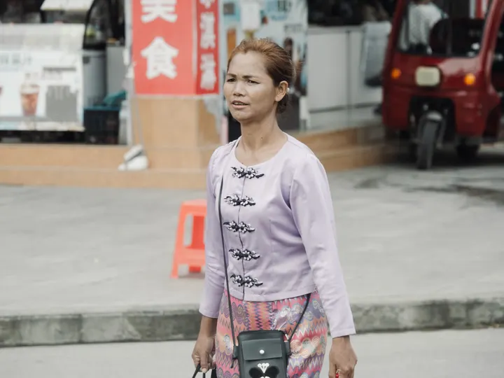 一位年轻女子抱着一个箱子 拿着相机在街上走