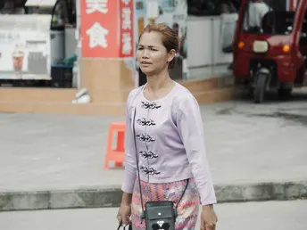 一位年轻女子抱着一个箱子 拿着相机在街上走