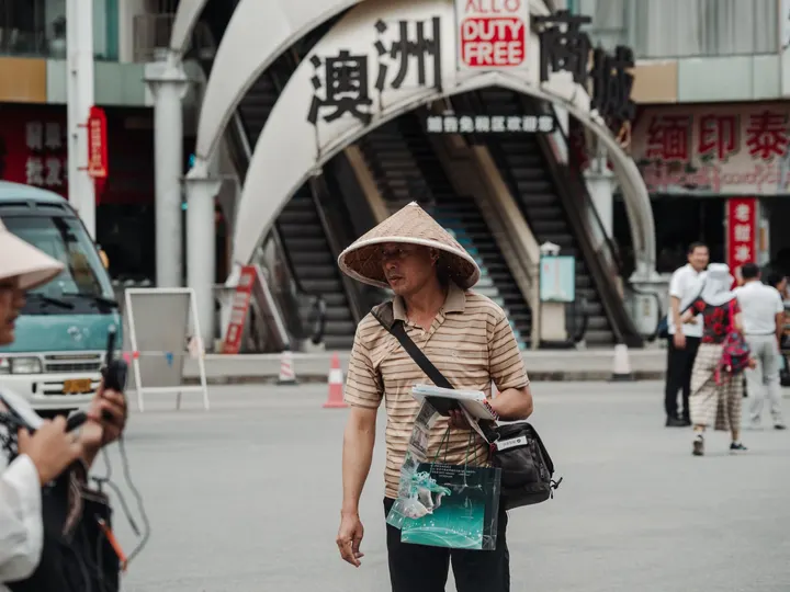一位戴帽子女士手持相机走在大城市街道上