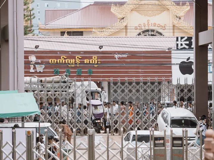 一个有围墙的街道 有汽车和行人 一只狗站在一扇门后面。