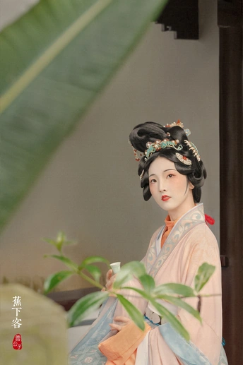 一位女性站在一株植物旁边 手里拿着一杯东西。