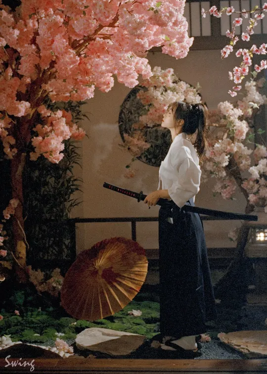 一位穿着和服的女性拿着雨伞靠近一棵开满粉色花朵的树。