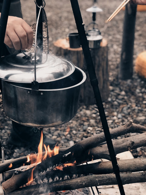 一个人在火上用木棍和热水壶烹饪食物
