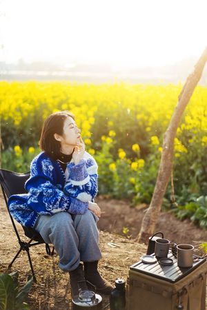 一位年轻女子坐在一片黄花的田野里的一把椅子上